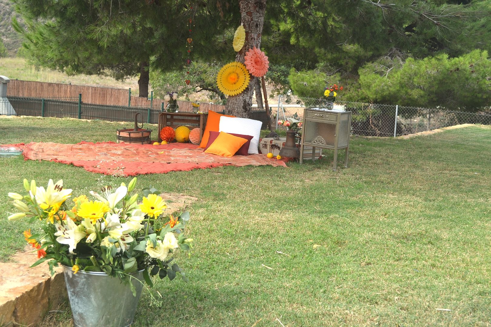  centro de flores en amarillo en cubo de metal y al fondo zona chill out de una boda en el jardín